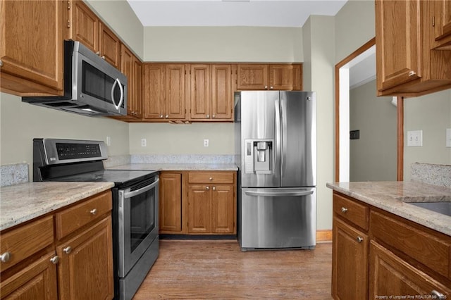 kitchen featuring brown cabinets, light stone countertops, light wood-style flooring, and stainless steel appliances