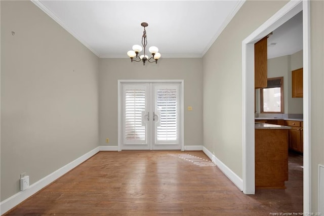 unfurnished dining area with french doors, crown molding, an inviting chandelier, and wood finished floors