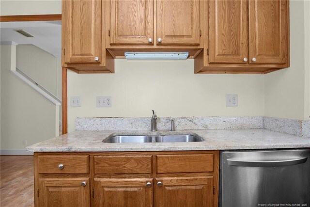 kitchen with light stone counters, brown cabinets, dishwasher, and a sink