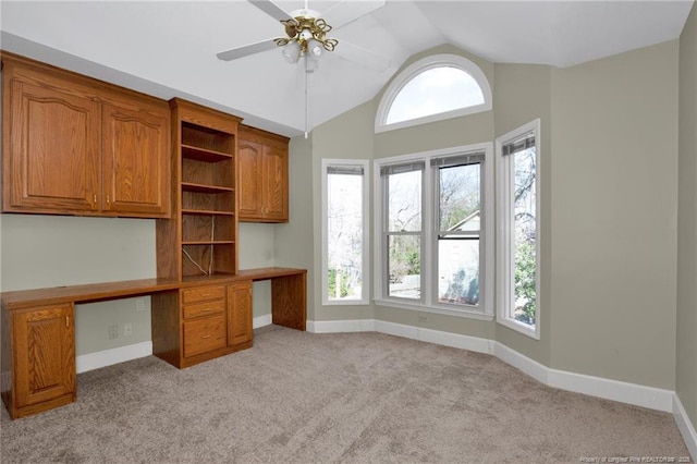 unfurnished office featuring ceiling fan, light carpet, baseboards, vaulted ceiling, and built in study area