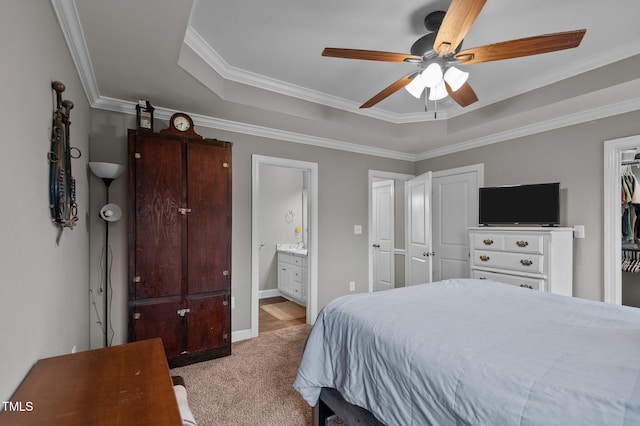 carpeted bedroom with crown molding, a raised ceiling, a ceiling fan, ensuite bath, and baseboards