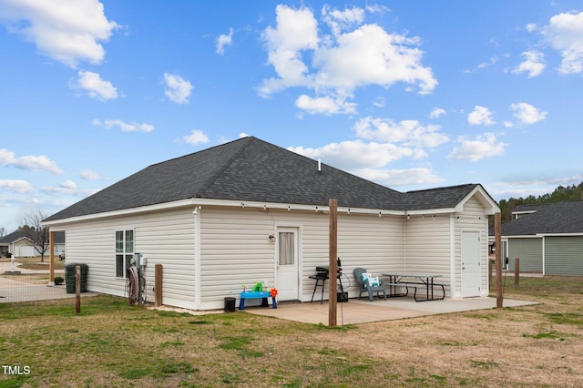 back of house with a shingled roof, a lawn, and a patio area