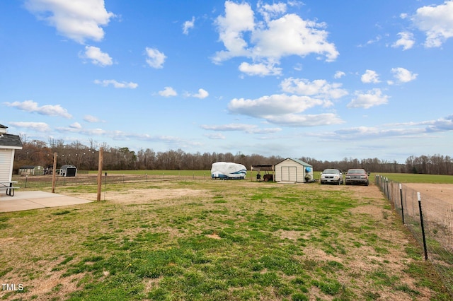 view of yard featuring a storage shed, a rural view, fence, and an outdoor structure