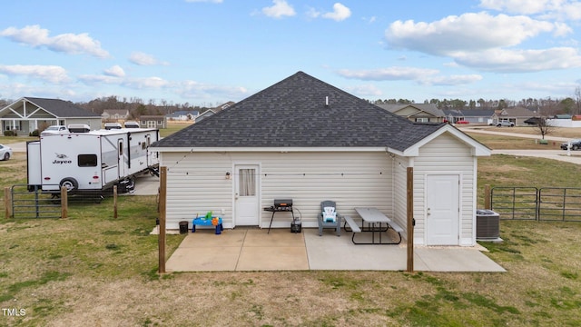 rear view of house with roof with shingles, fence, a lawn, and a patio