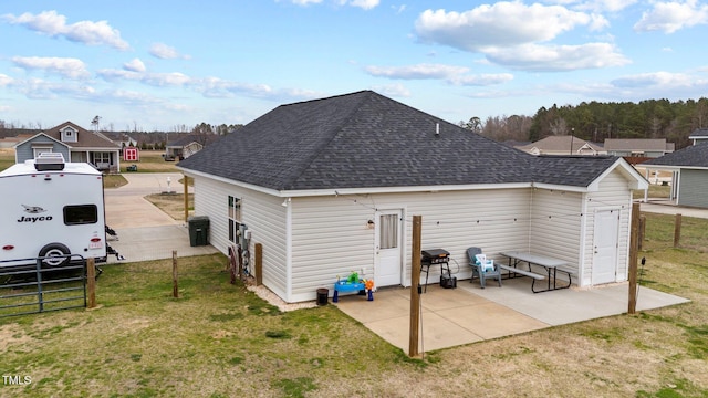 back of property with a shingled roof, a yard, fence, and a patio