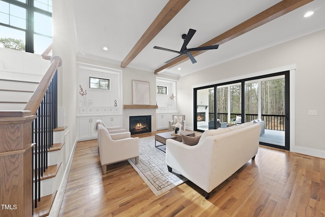 living area featuring light wood finished floors, a warm lit fireplace, and beamed ceiling