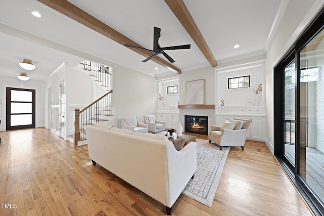 living area with a glass covered fireplace, light wood-style flooring, stairway, beamed ceiling, and recessed lighting