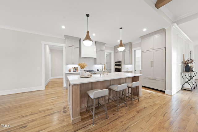 kitchen with ornamental molding, a kitchen breakfast bar, a kitchen island with sink, light countertops, and light wood-type flooring