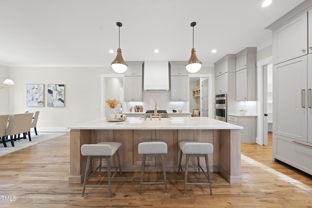 kitchen with an island with sink, stainless steel double oven, light wood-style flooring, and a breakfast bar area