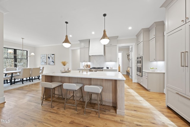 kitchen featuring custom range hood, ornamental molding, a kitchen breakfast bar, light countertops, and light wood-style floors