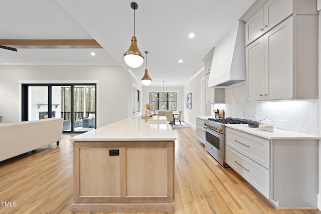 kitchen with stainless steel range, tasteful backsplash, light wood-style floors, open floor plan, and premium range hood