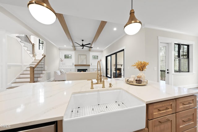 kitchen with light stone counters, a sink, open floor plan, a lit fireplace, and beamed ceiling