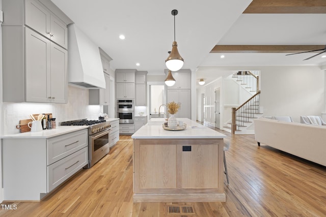 kitchen featuring light wood-style flooring, open floor plan, custom exhaust hood, stainless steel appliances, and light countertops