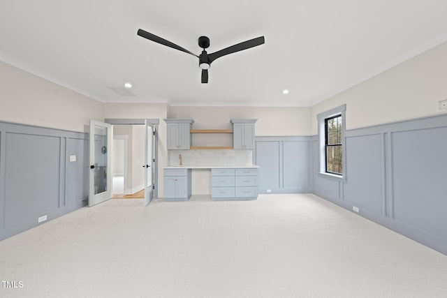 unfurnished living room with light carpet, built in desk, crown molding, and a decorative wall