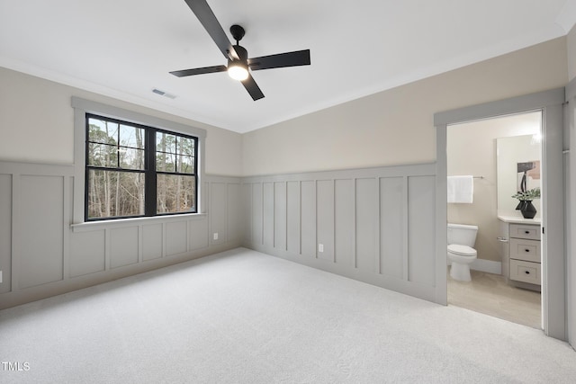 unfurnished bedroom featuring carpet floors, a wainscoted wall, crown molding, visible vents, and ensuite bath