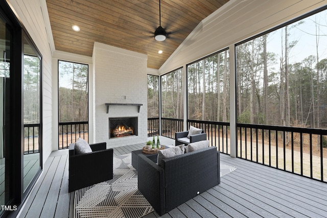 sunroom / solarium with wood ceiling, ceiling fan, vaulted ceiling, a brick fireplace, and a wooded view