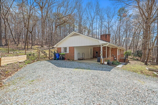 view of home's exterior featuring brick siding, an attached carport, driveway, and a chimney