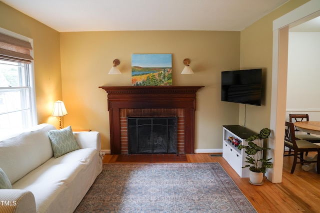 living room featuring a brick fireplace, baseboards, and wood finished floors