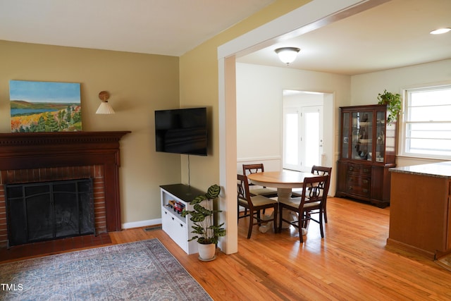 dining area with baseboards, a brick fireplace, and light wood finished floors