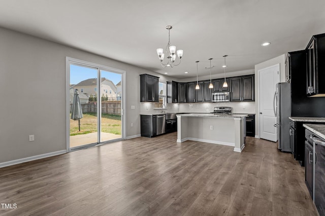 kitchen with wood finished floors, an inviting chandelier, stainless steel appliances, decorative backsplash, and a center island