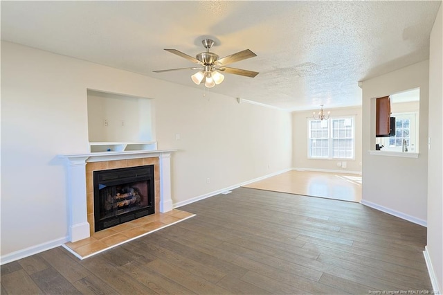 unfurnished living room with baseboards, wood finished floors, a textured ceiling, a fireplace, and ceiling fan with notable chandelier