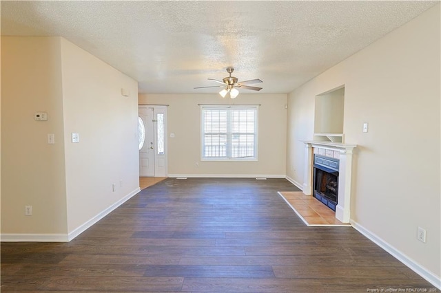 unfurnished living room featuring ceiling fan, dark wood finished floors, a textured ceiling, and a tile fireplace