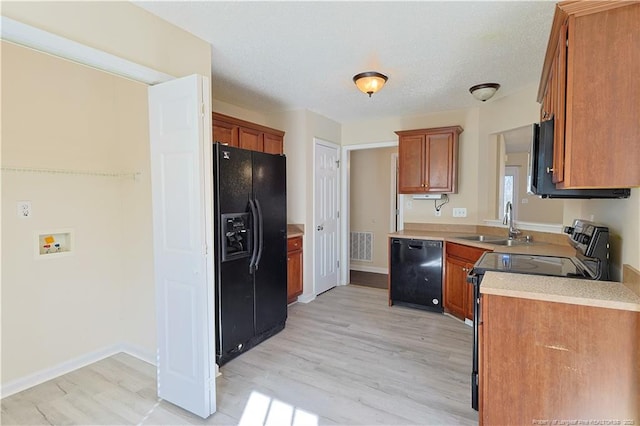 kitchen featuring light wood finished floors, brown cabinets, light countertops, black appliances, and a sink