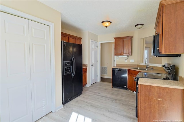 kitchen featuring black appliances, a sink, light countertops, and brown cabinets