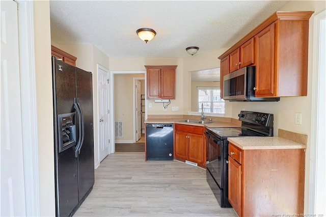 kitchen featuring brown cabinets, light countertops, visible vents, a sink, and black appliances