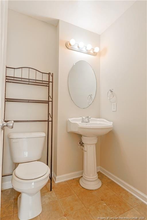 half bathroom with toilet, baseboards, and tile patterned floors