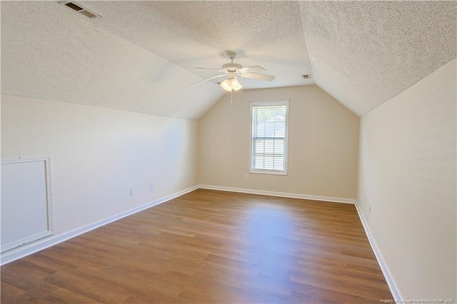 additional living space with a textured ceiling, vaulted ceiling, wood finished floors, and visible vents