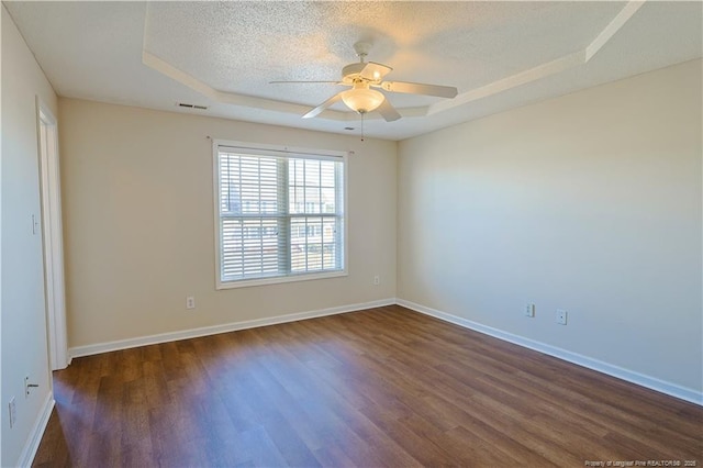 empty room featuring a textured ceiling, dark wood-style flooring, visible vents, baseboards, and a tray ceiling