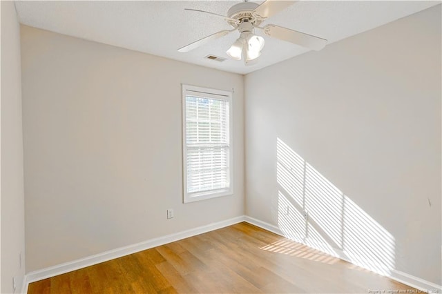 empty room with a ceiling fan, wood finished floors, visible vents, and baseboards