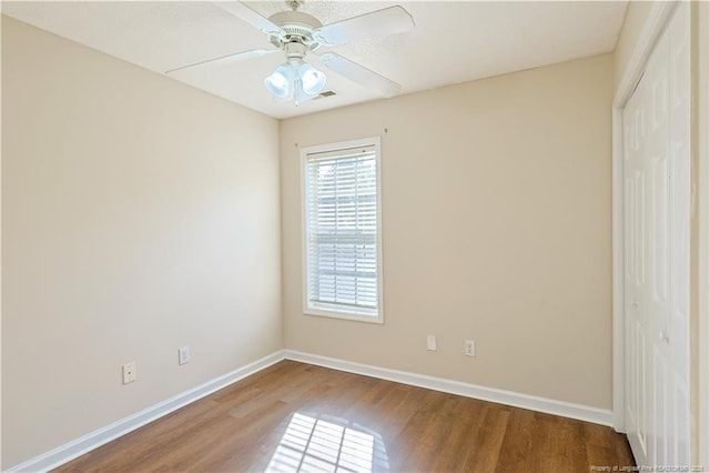 empty room featuring ceiling fan, visible vents, baseboards, and wood finished floors