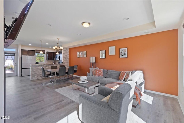 living room with baseboards, recessed lighting, an inviting chandelier, and light wood-style floors