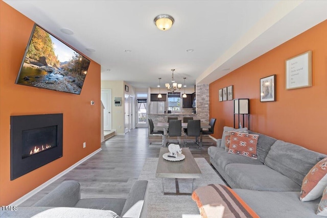 living room featuring an inviting chandelier, a lit fireplace, baseboards, and wood finished floors