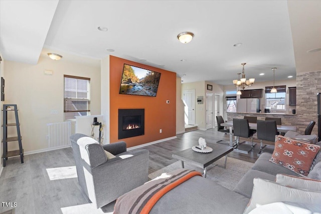 living room with a warm lit fireplace, light wood-type flooring, baseboards, and a notable chandelier