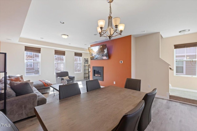 dining area featuring a notable chandelier, baseboards, wood finished floors, and a glass covered fireplace