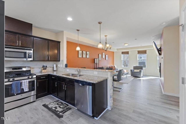 kitchen featuring light wood finished floors, open floor plan, a peninsula, stainless steel appliances, and a sink