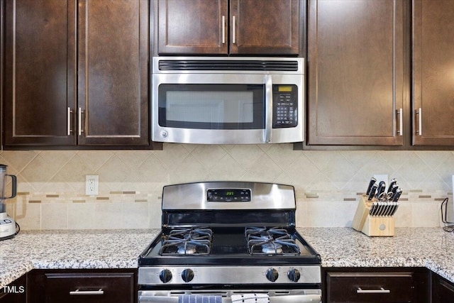 kitchen with dark brown cabinets, appliances with stainless steel finishes, light stone counters, and tasteful backsplash