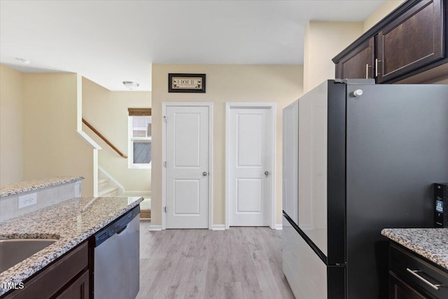 kitchen with light stone counters, light wood finished floors, stainless steel dishwasher, freestanding refrigerator, and dark brown cabinets