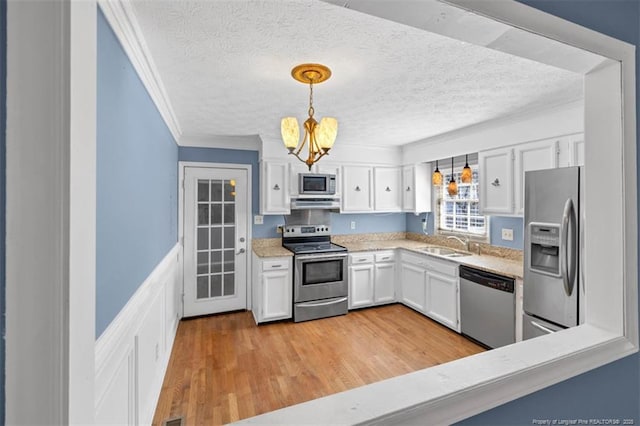 kitchen featuring a sink, light countertops, appliances with stainless steel finishes, ornamental molding, and light wood finished floors