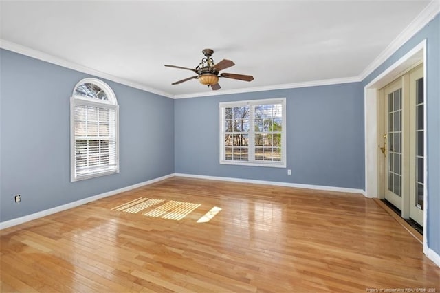 spare room with ornamental molding, a wealth of natural light, light wood-style floors, and baseboards