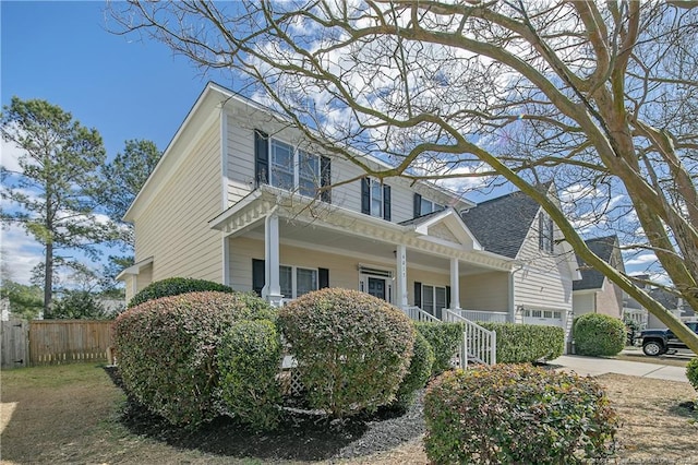 view of side of property with covered porch, concrete driveway, fence, and a garage