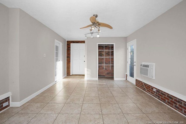 spare room featuring light tile patterned floors, a ceiling fan, an AC wall unit, brick wall, and baseboards