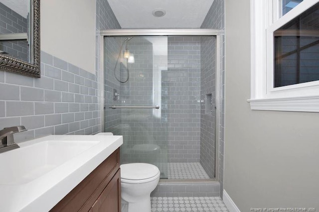 bathroom featuring toilet, tile patterned floors, vanity, a shower stall, and tile walls