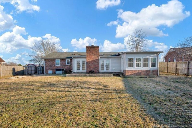 rear view of property with a fenced backyard, brick siding, french doors, a lawn, and a chimney