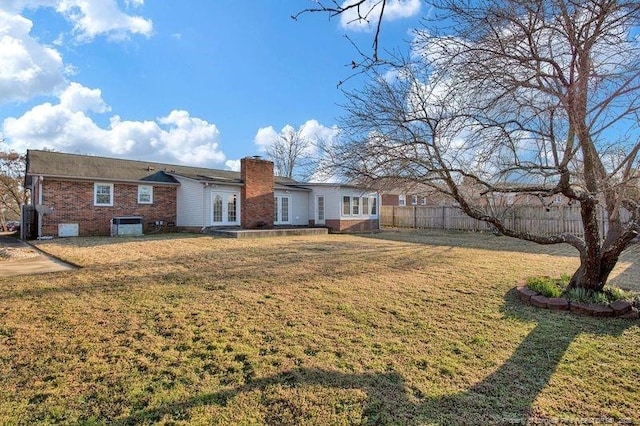 back of property with brick siding, fence, a yard, french doors, and a chimney