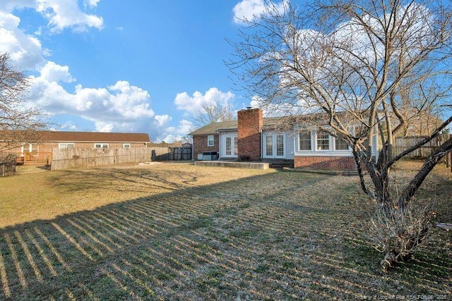 rear view of house with brick siding, fence, a yard, french doors, and a chimney