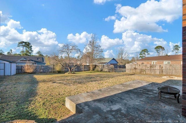 view of yard featuring a storage shed, a fenced backyard, and an outdoor fire pit